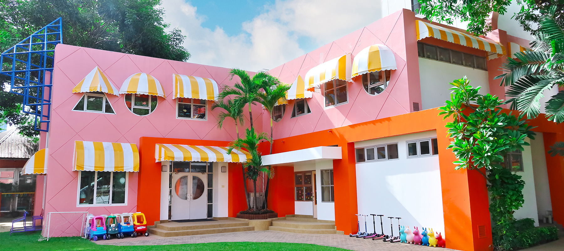 タイ・バンコクにあるメロディー幼稚園・ナーサリーの園舎外観。ピンクとオレンジの明るい建物と広い芝生の園庭